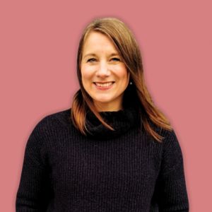 Eine Frau mit glattem braunem Haar, die einen schwarzen Rollkragenpullover trägt, lächelt selbstbewusst, während sie vor einem schlichten rosa Hintergrund steht - perfekt, um Dienste wie "Mitgliederbereich erstellen lassen" vorzustellen.