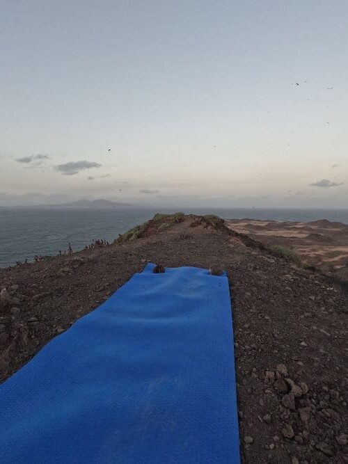 Blaue Yogamatte ausgerollt auf einem Berg mit erdigem Untergrund und Ausblick auf's Meer und die Insel Lanzarote
